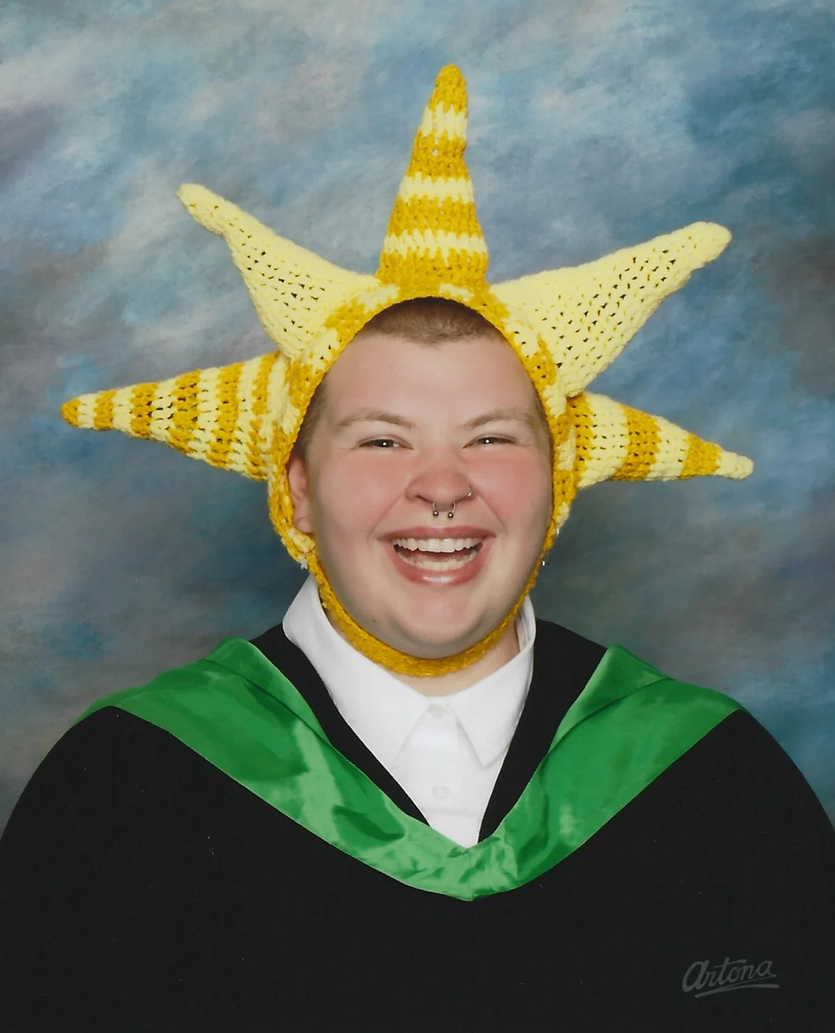 Theo Falkiner smiling in graduation robes and a handmade sun hat
